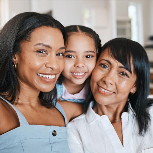 Smiling African American daughter, granddaughter, and grandmother taking selfie on couch