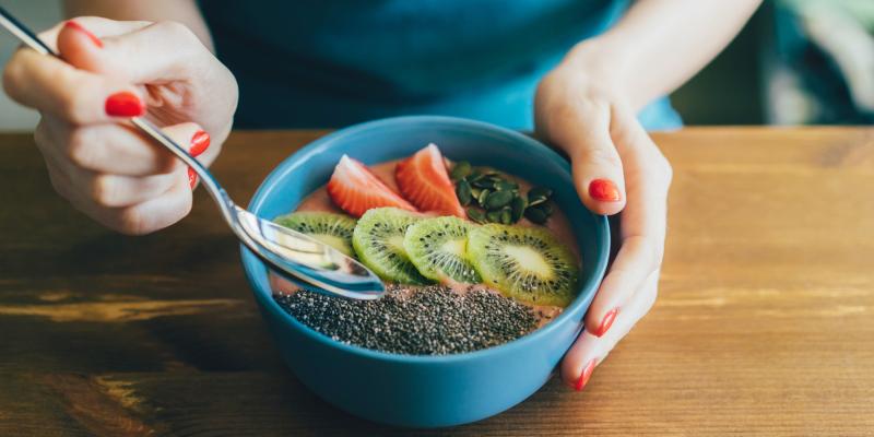 woman eating a healthy meal of fruits and yogurt in blue bowl