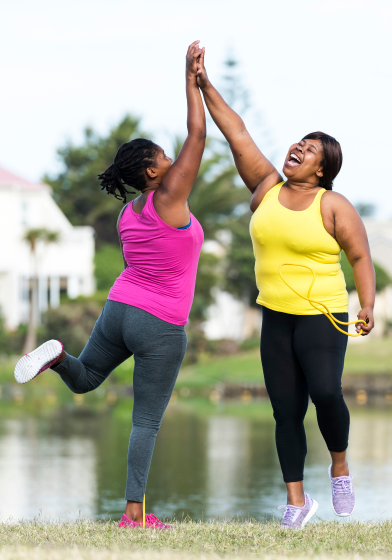 Two women wearing exercise clothes high-five while outside.
