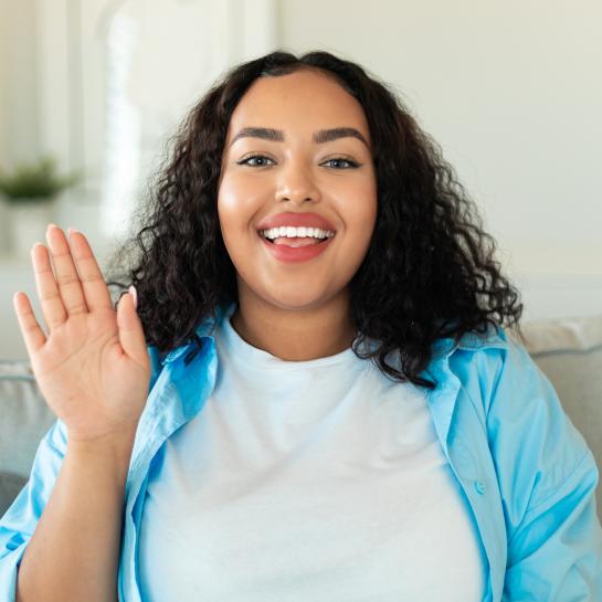 Communities of Color- happy black lady waving hello sitting on sofa