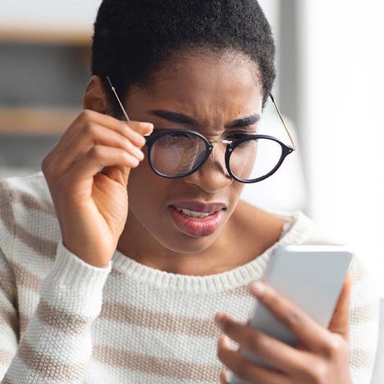 African American woman with glasses squinting to look at her phone screen