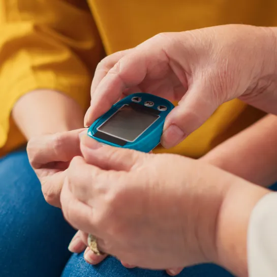 Doctor checking a young person's blood glucose using a blue glucometer.