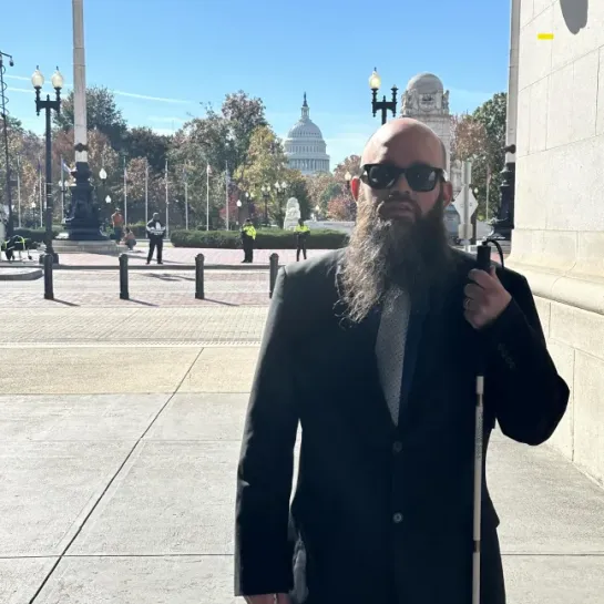 Blind man with beard, sunglasses, and white cane outside the U.S. Capitol.
