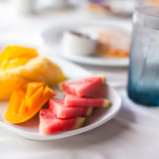Sliced watermelon, persimmon, and pineapple on a plate with a glass of water.