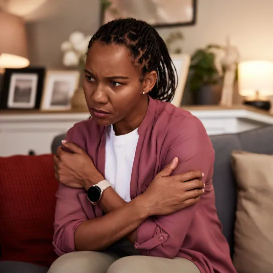 Woman on sofa, hugging herself, looking distressed and uncomfortable.