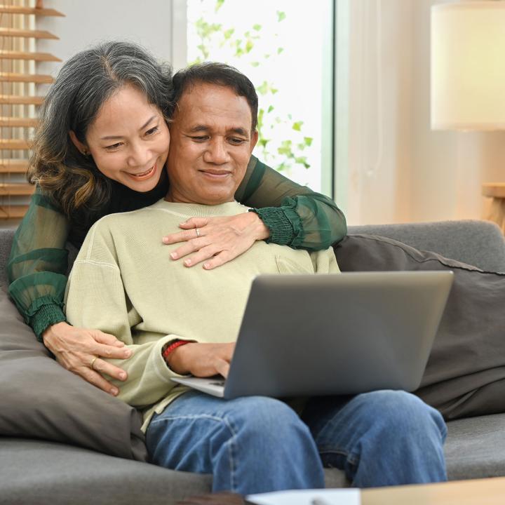 Senior Asian couple on couch looking at laptop computer