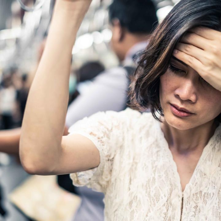 Asian woman on subway feeling ill with hand on forehead