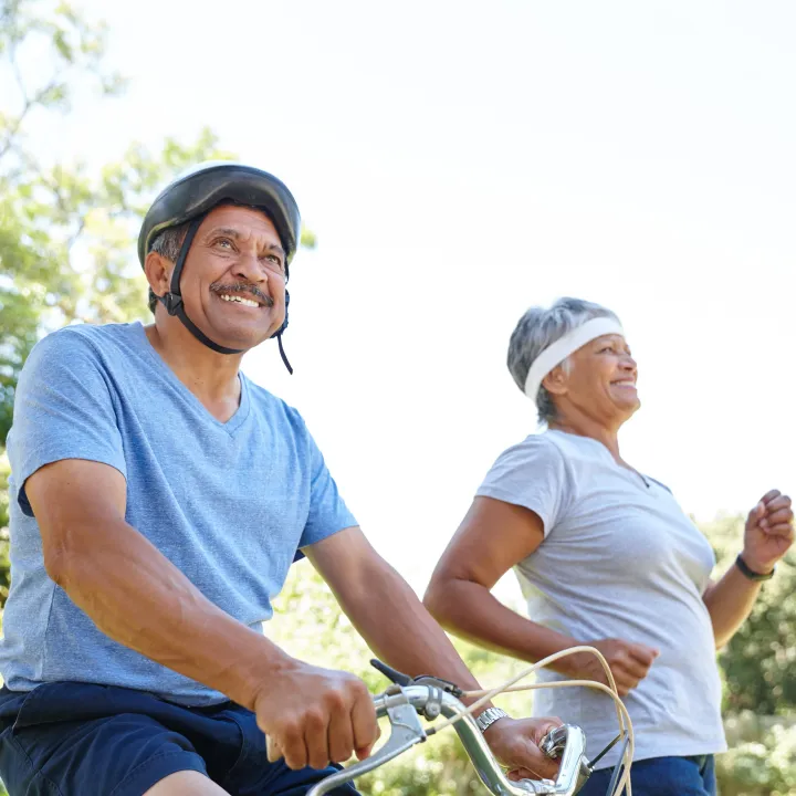 A happy elderly couple out on a sunny day, the man on a bicycle and the woman jogging