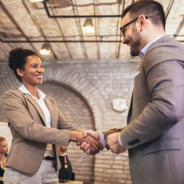 Businesswoman and businessman shaking hands in office setting.