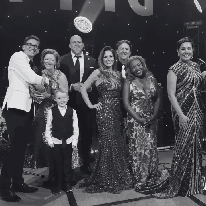 Diverse group, including a child, in formal attire smiling on stage at a gala.