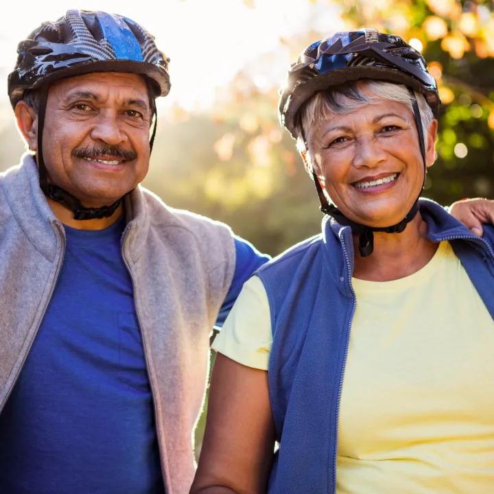 Hombre y mujer mayores, sonrientes, con cascos de bicicleta al aire libre.py