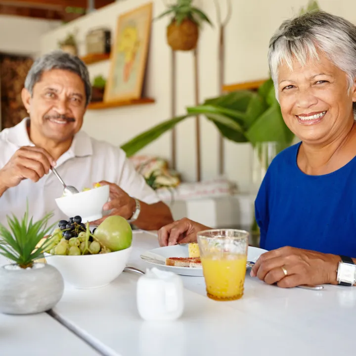 Pareja de adultos mayores sonriendo, disfrutando de un desayuno saludable con fruta.