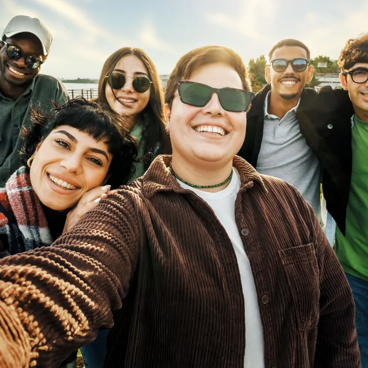 Diverse group of six smiling young adults taking a selfie outdoors.