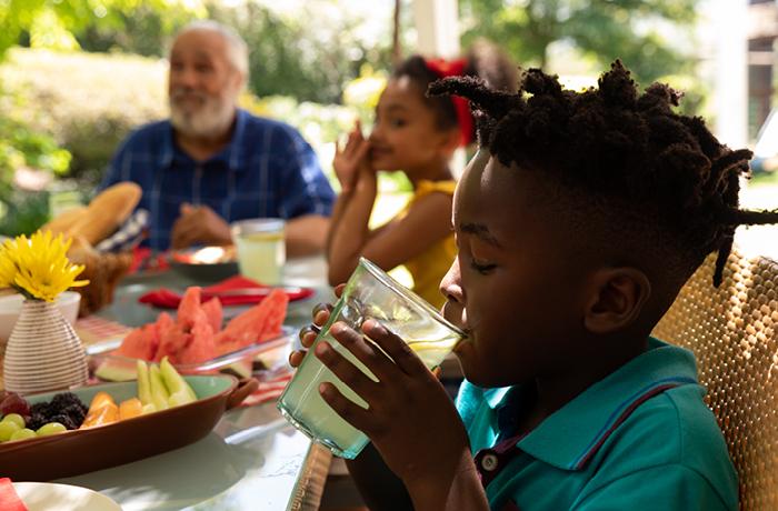 Young African American boy drinking lemonade at table outdoors with family