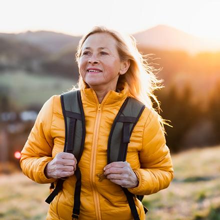 Middle-age Latina woman hiking outdoors with backpack and yellow coat