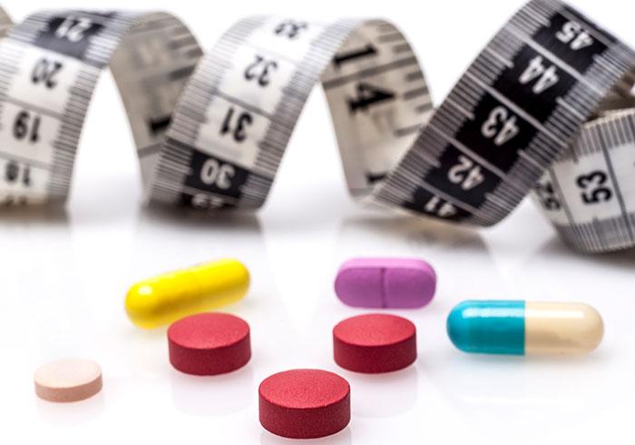 Various brightly-colored pills in front of coiled black and white measuring tape