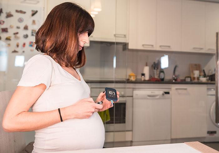 Pregnant woman with gestational diabetes checking her blood glucose level in kitchen