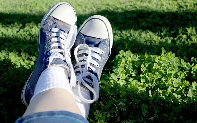 Close-up of woman stretching out her feet wearing blue tennis shoes atop green clover on sunny day