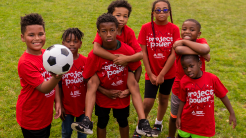 Group of African American children wearing project power shirts and playing soccer