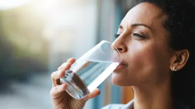 African American woman drinking a tall glass of water by the window