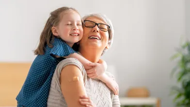 senior woman smiling with a band-aid on her arm and hugging her grandchild