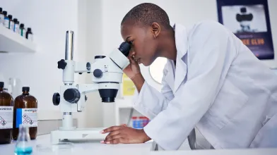 African American woman researcher leaning on desk and looking in microscope