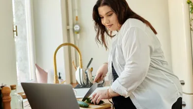 Heavy set woman in kitchen watching a recipe video while chopping vegetable
