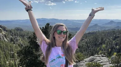 A woman on a mountain top with her arms raised.