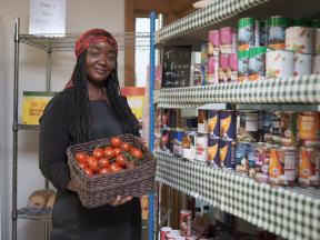 african american woman standing in food pantry holding a basket of tomatoes