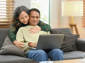 Senior Asian couple on couch looking at laptop computer