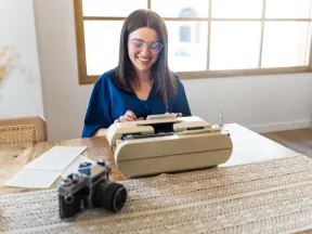 Young woman typing on a typewriter at desk with slr camera sitting on table