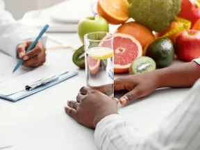 African American woman with glass of water near fruit talking to nutritionist