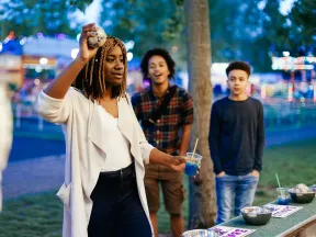 A woman holds up a ball about to throw it at a fundraiser game with two young men looking on in the background.