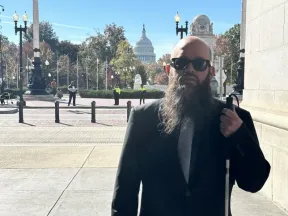 Blind man with beard, sunglasses, and white cane outside the U.S. Capitol.