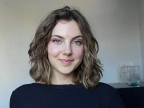 Smiling young woman with wavy brown hair and blue eyes in a black top.