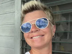 Smiling woman with short blonde hair, wearing reflective sunglasses.