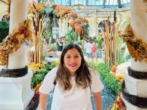 Woman smiles in an indoor garden decorated with autumn leaves and pumpkins.