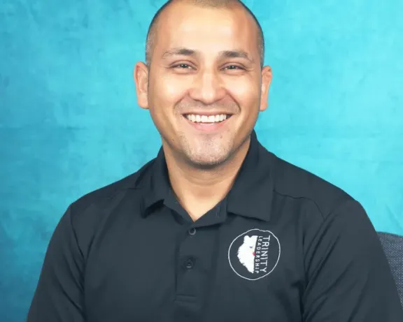 Smiling man in a black polo shirt against a textured blue background.