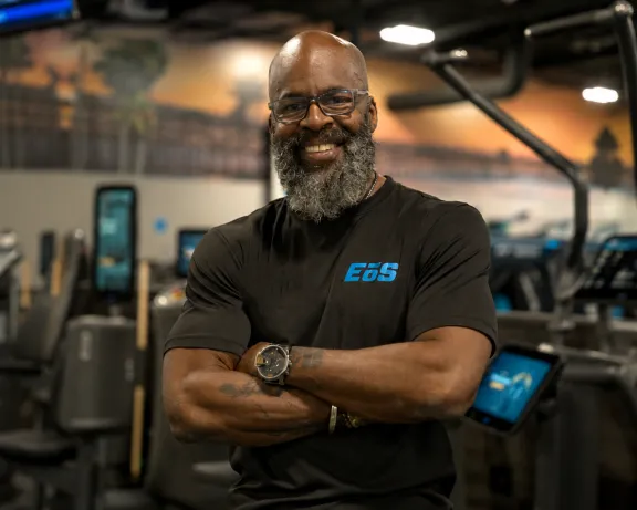 Confident man with beard smiles, arms crossed, in a modern gym.