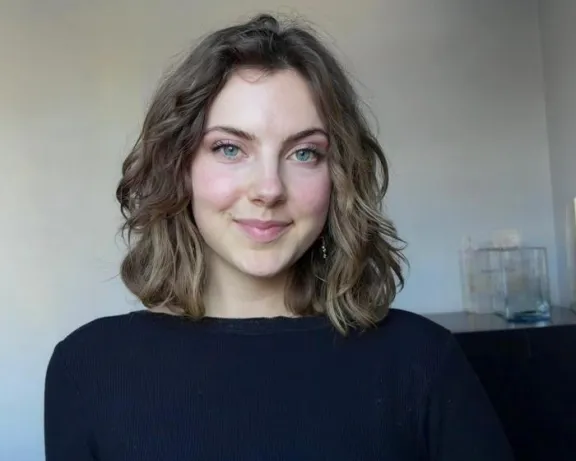 Smiling young woman with wavy brown hair and blue eyes in a black top.