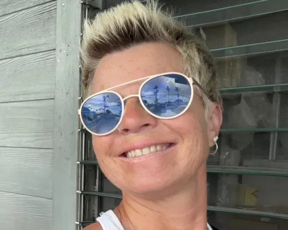 Smiling woman with short blonde hair, wearing reflective sunglasses.