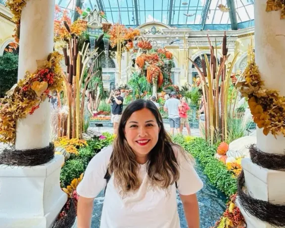 Woman smiles in an indoor garden decorated with autumn leaves and pumpkins.
