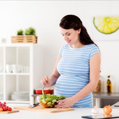 Pregnant woman making salad in kitchen