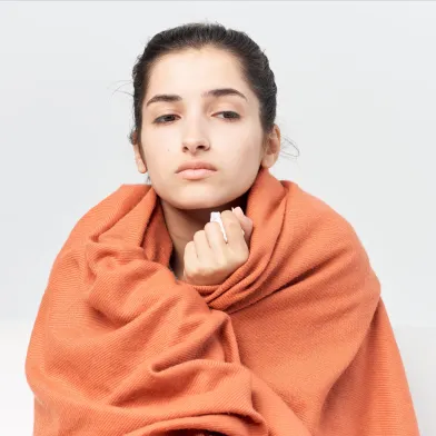 Teenage girl with cold wrapped in blanket to keep warm