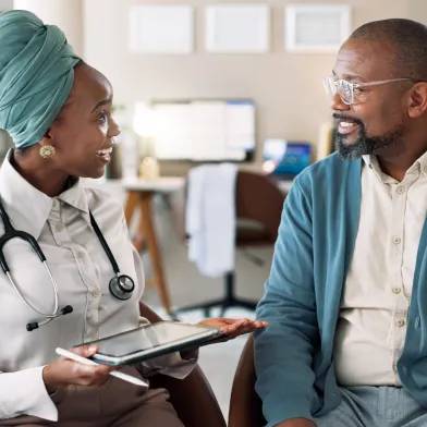 Female doctor with a headwrap reviews tablet with a male patient in a clinic.