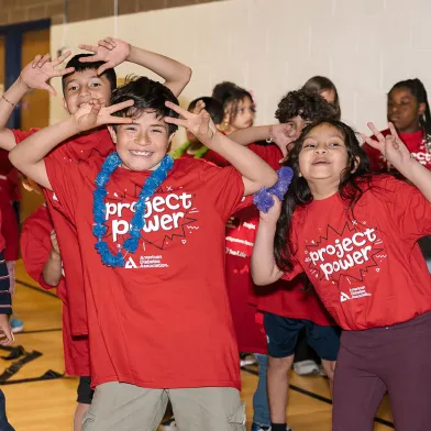 Happy children in red "project power" shirts making playful gestures in a gym.