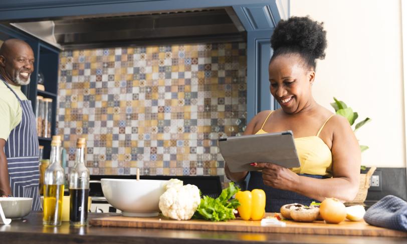 Happy African American couple looking at tablet and preparing dinner in kitchen