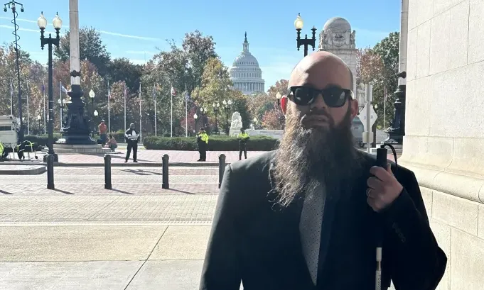 Blind man with beard, sunglasses, and white cane outside the U.S. Capitol.