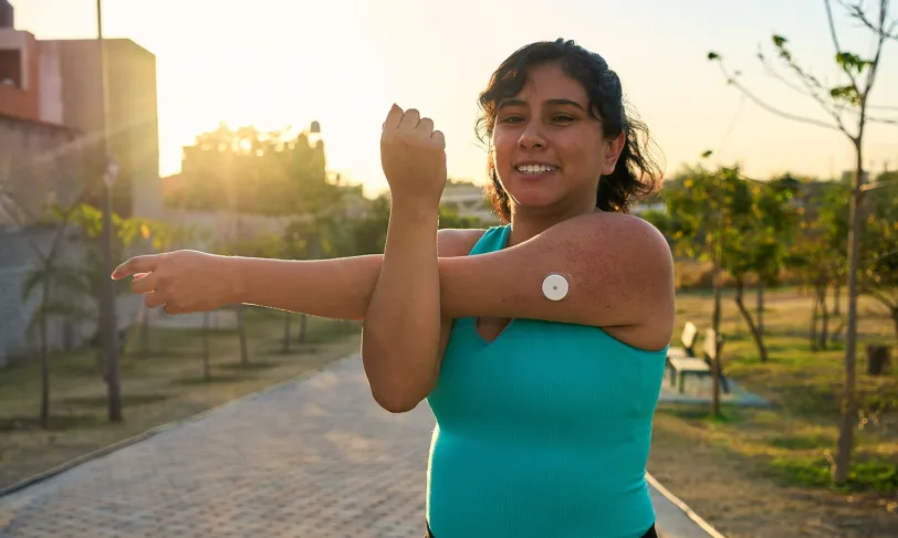 Happy woman stretching outdoors with a continuous glucose monitor on her arm.