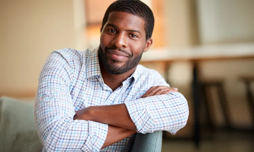 Smiling Black man with crossed arms in a plaid shirt.